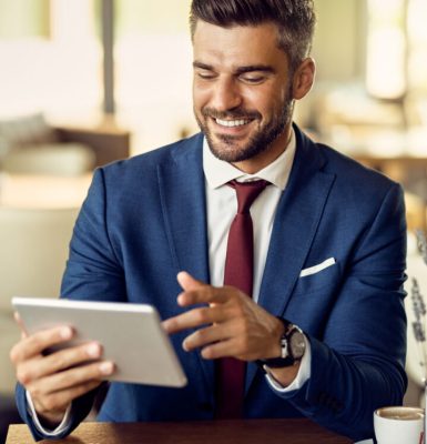 Happy entrepreneur making video call over touchpad during his coffee break in a cafe,